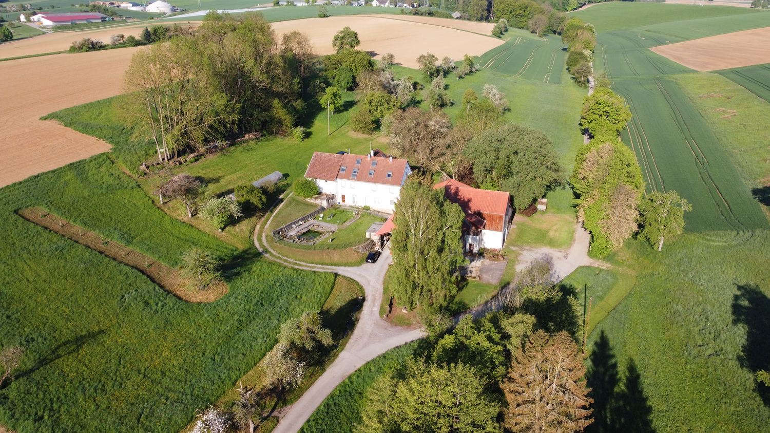 Luftbild des Hofs mit Wohnhaus, Scheune, umliegenden Feldern und Biogas-Anlage im Hintergrund